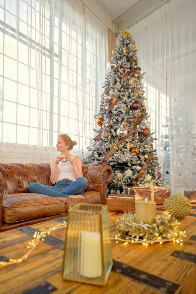 Woman relaxing on a sofa with a cup of tea in a cozy living room beside a decorated Christmas tree and festive holiday decor Woman relaxing on a sofa with a cup of tea in a cozy living room beside a decorated Christmas tree and festive holiday decor